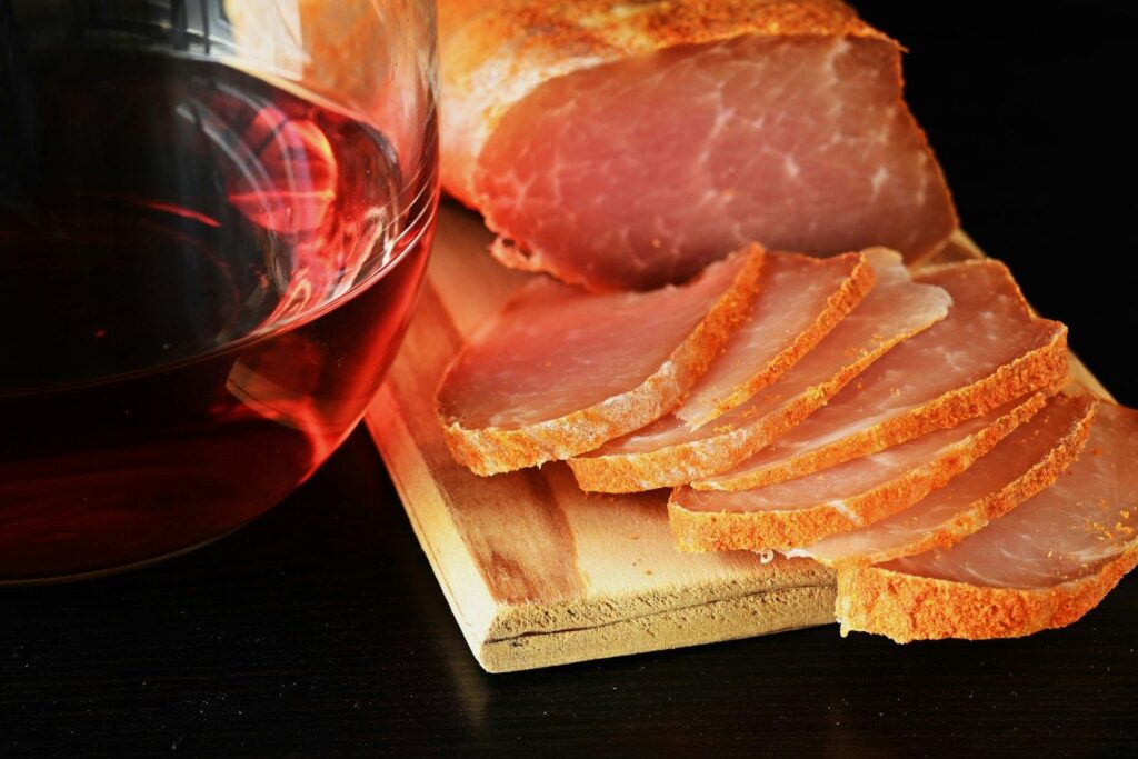 Tranches de rôti de porc sur une planche en bois à côté d'un verre de vin rouge