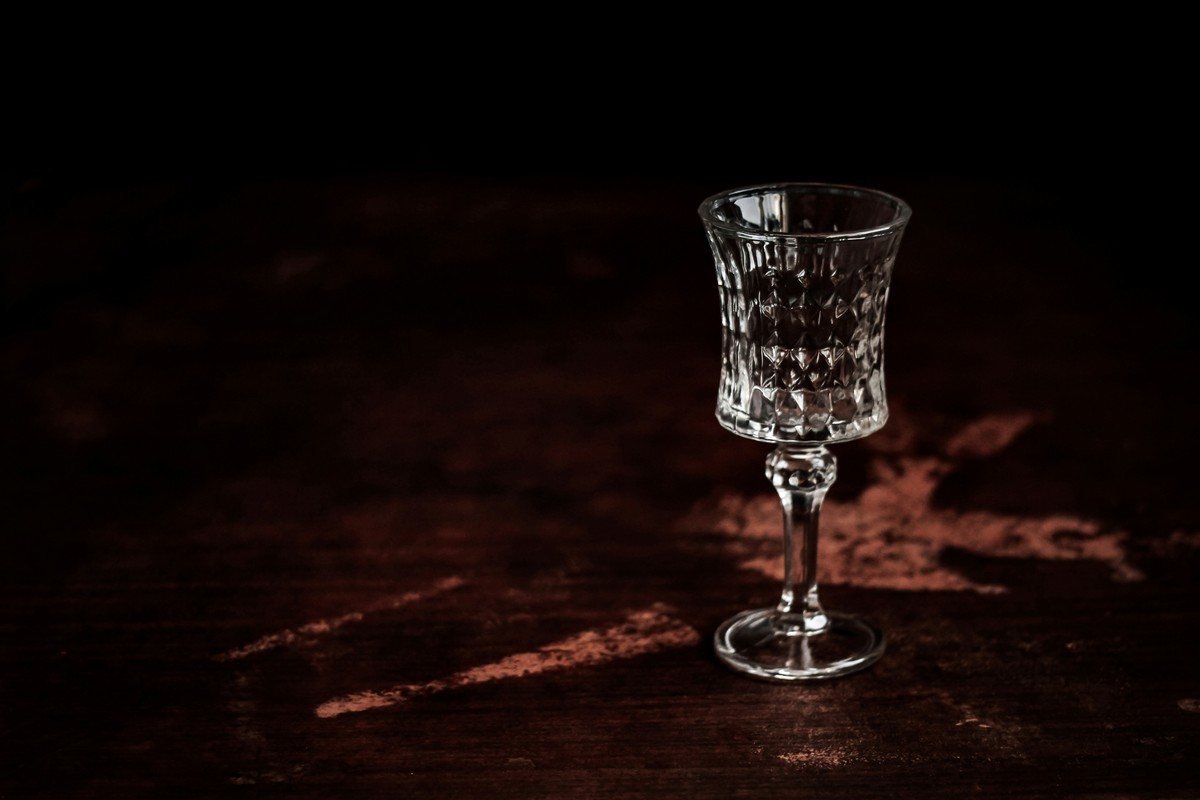 Petit verre en cristal taillé posé seul sur une table en bois sombre